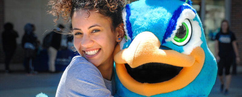 Female student smiling and hugging the peacock mascot.